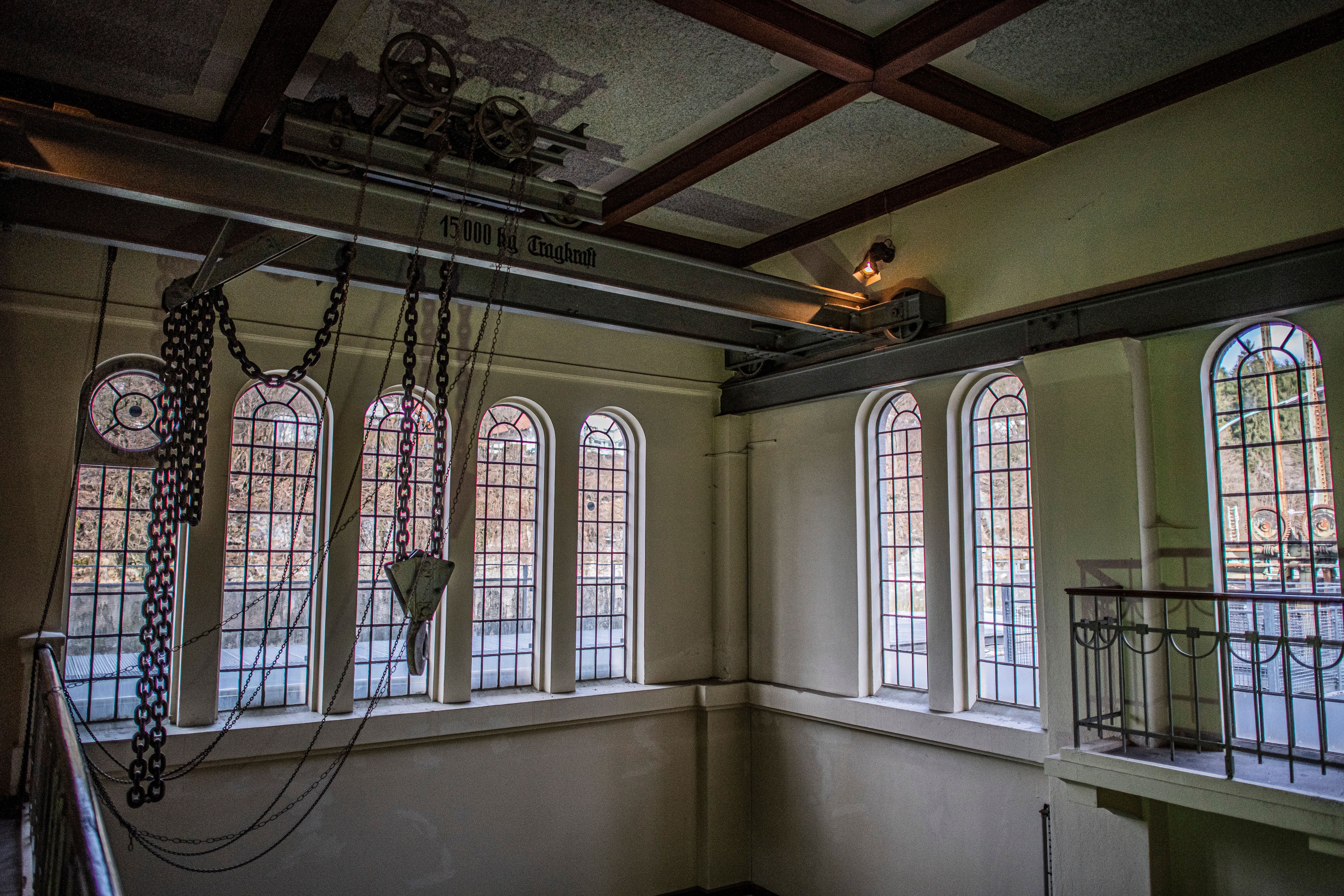 Historische Krananlage mit Kettenzug im Schaukraftwerk Schwellöd vor hohen Rundbogenfenstern der ehemaligen Maschinenhalle.