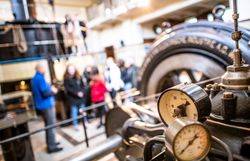 Manometer und historische Maschinentechnik im Schaukraftwerk Schwellöd, während Besucher an einer Führung durch das denkmalgeschützte Wasserkraftwerk teilnehmen.